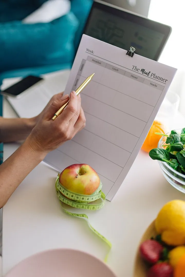 Planificador semanal de comidas con fruta y verdura fresca sobre la mesa